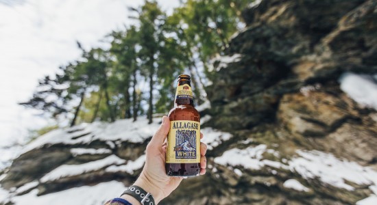 Allagash White in Mountains beverage being held in the air outside